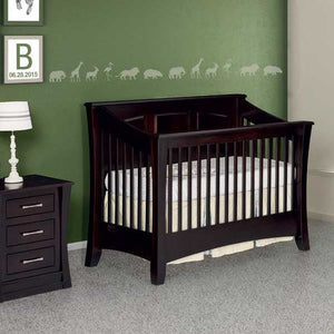 Espresso convertible baby crib with slatted sides and arched panel headboard staged in a green nursery beside a nightstand