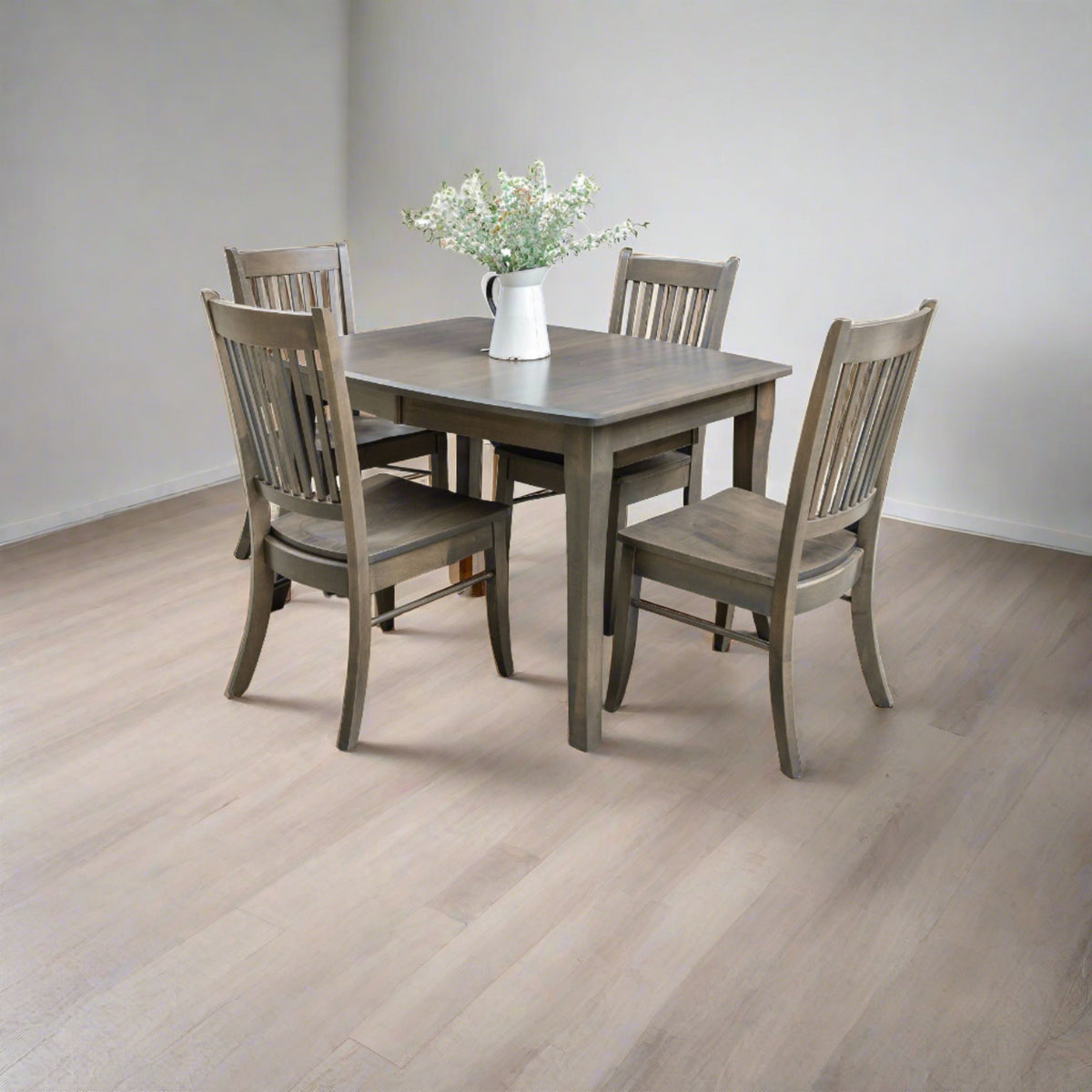 Compact gray dining table with four slat back chairs in a bright room with light plank flooring