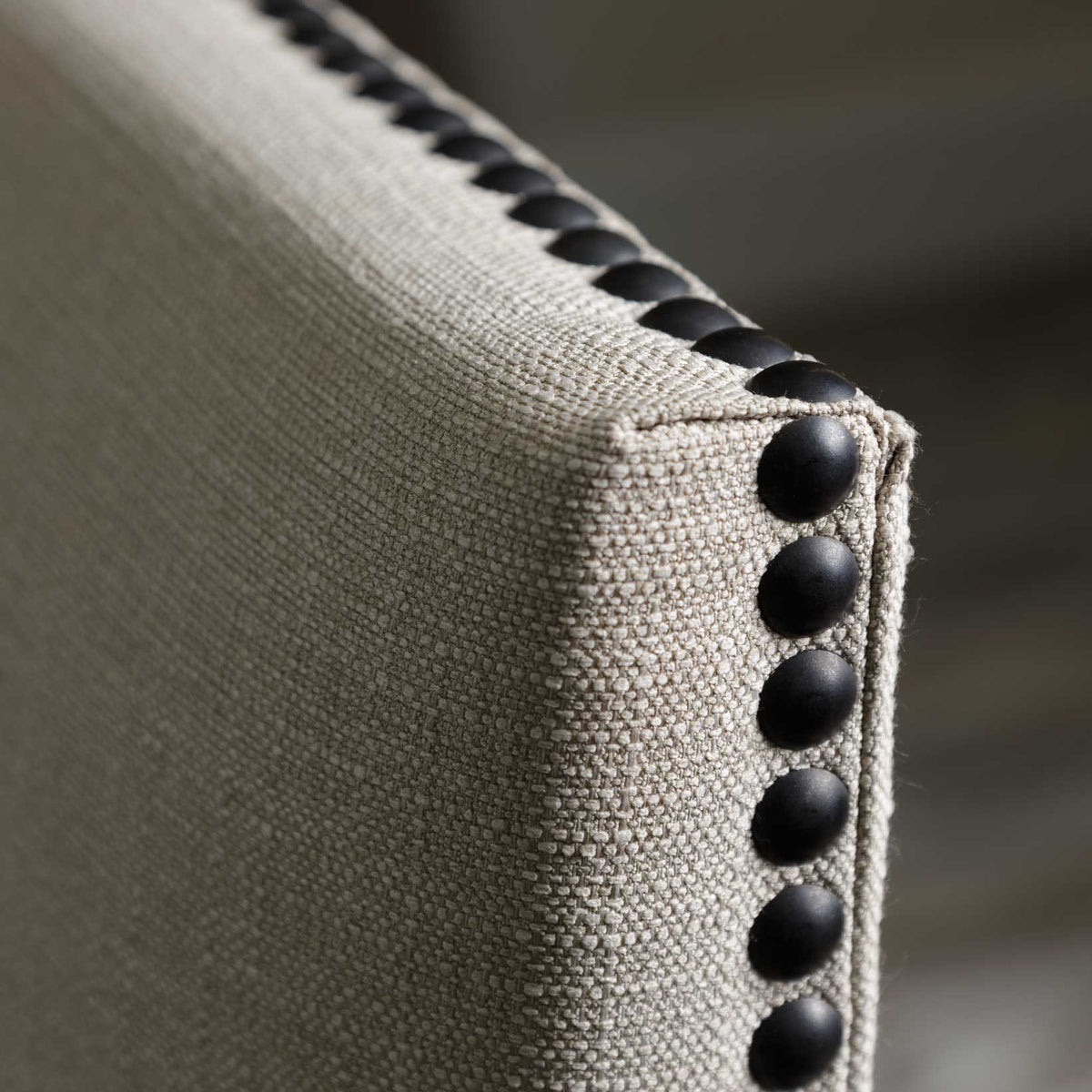 Macro view of the woven oatmeal linen upholstery and row of black dome nailhead studs on the chair back