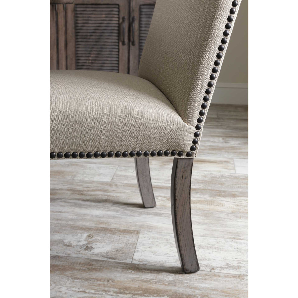 Detail of the upholstered dining chair showing black nailhead trim along the seat and curved weathered gray legs
