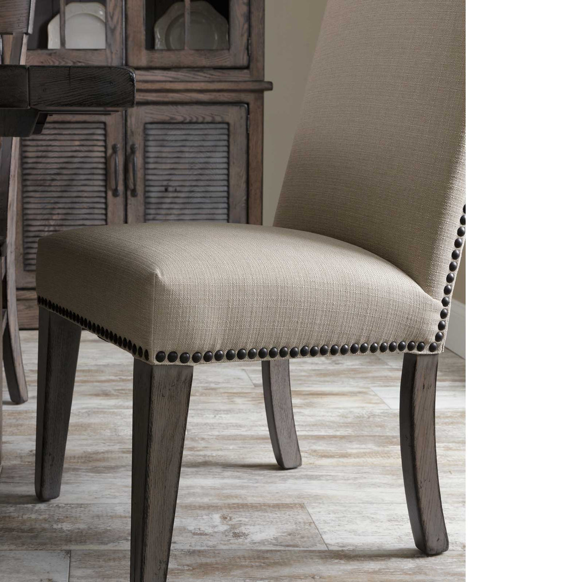 Close-up of the linen dining chair seat and dark nailhead studs with a louvered wood cabinet in the background