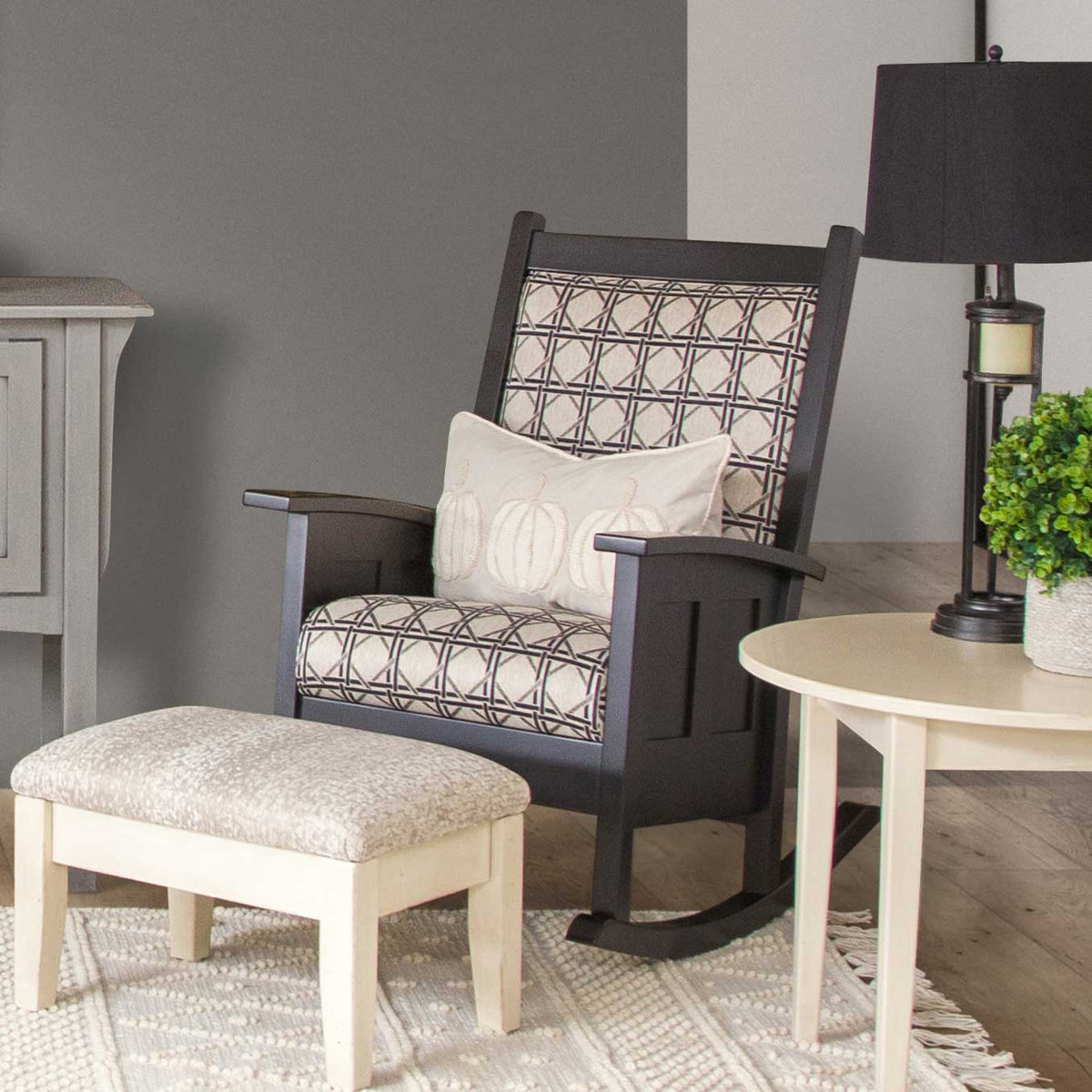 Black painted Shaker cushion rocking chair with patterned seat cushions beside an upholstered ottoman in a styled gray room