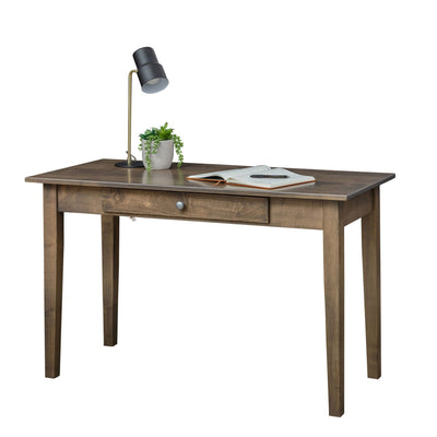 Gray brown Shaker writing desk with one wide drawer, tapered legs, black desk lamp, plant and open notebook on top