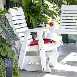 White poly glider chair with red seat cushion and sun hat on a shaded stone porch beside potted greenery