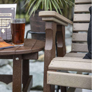 Close view of a weatherwood poly glider arm and slatted seat next to a brown round side table with iced tea