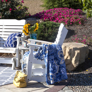 White poly glider chair and glider bench flanking a small side table with sunflowers in a landscaped garden
