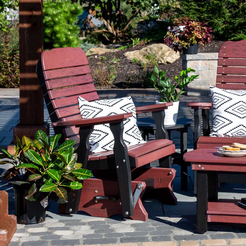 Cherry red and black poly glider chairs with geometric pillows and side tables on a paver patio garden