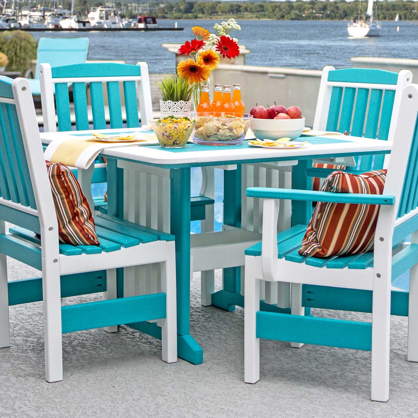 Aruba blue and white poly square patio dining table with four slat back arm chairs on a waterfront patio