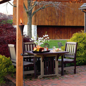 Weatherwood and cherry poly dining table for four under a pergola with tiki torch and barn in the background