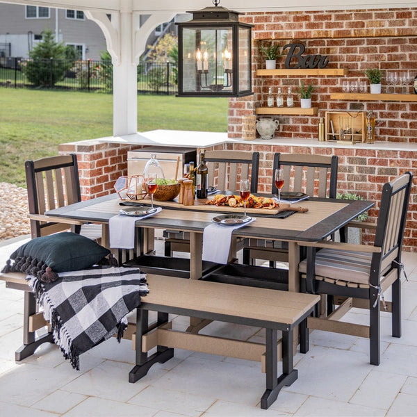 Weatherwood and black poly dining table with four chairs and two benches set for dinner in an outdoor bar pavilion