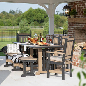 Weatherwood and gray poly dining table with cushioned chairs and a bench under a pavilion by a brick fireplace