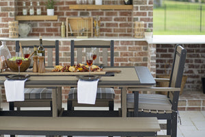 Close view of a weatherwood poly dining table set with plates, wine and a grilled platter beside striped seat cushions
