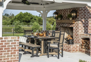 Weatherwood and gray poly dining table with cushioned arm chairs and a bench under a pavilion by a brick fireplace