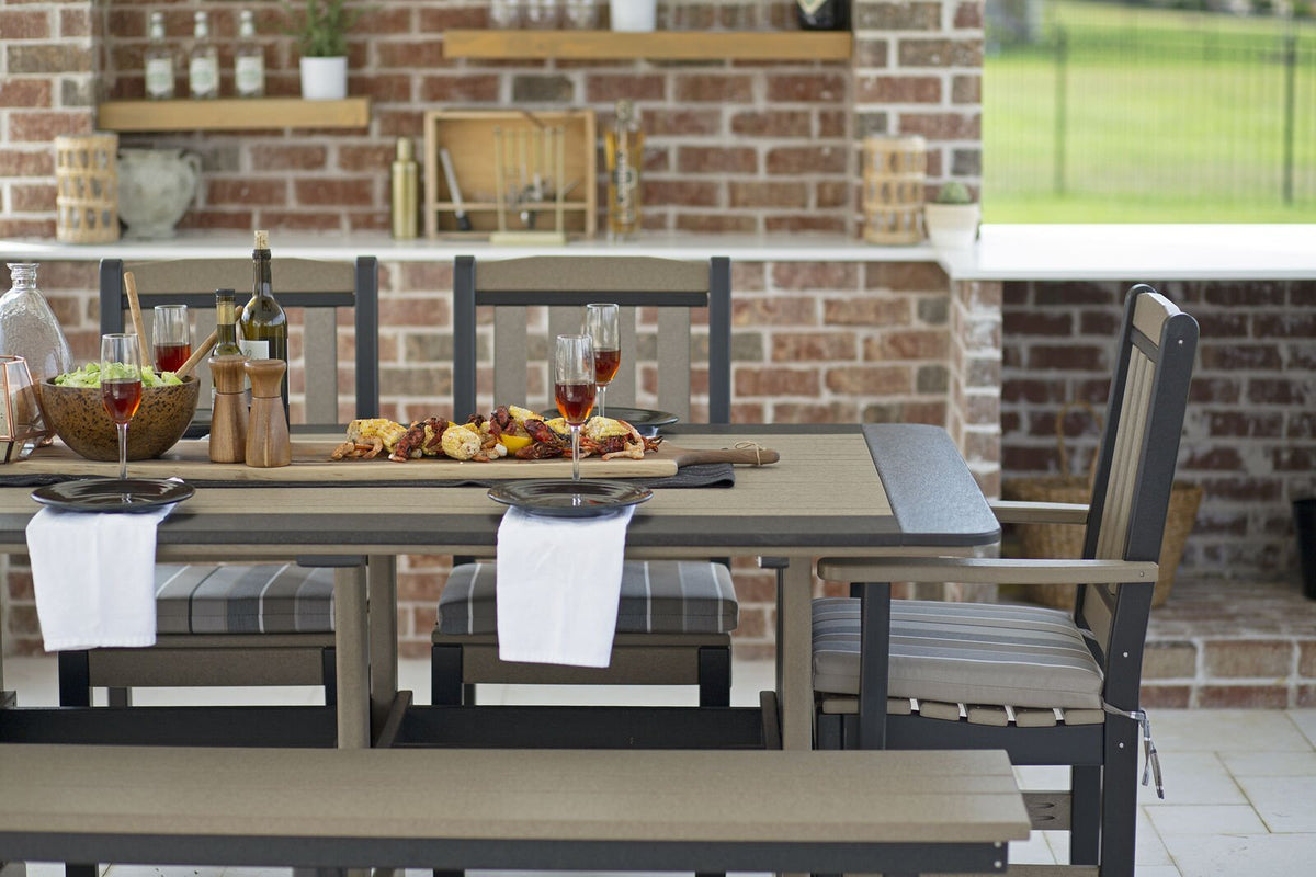Close view of a weatherwood poly dining table set with plates, wine and a grilled platter beside striped seat cushions