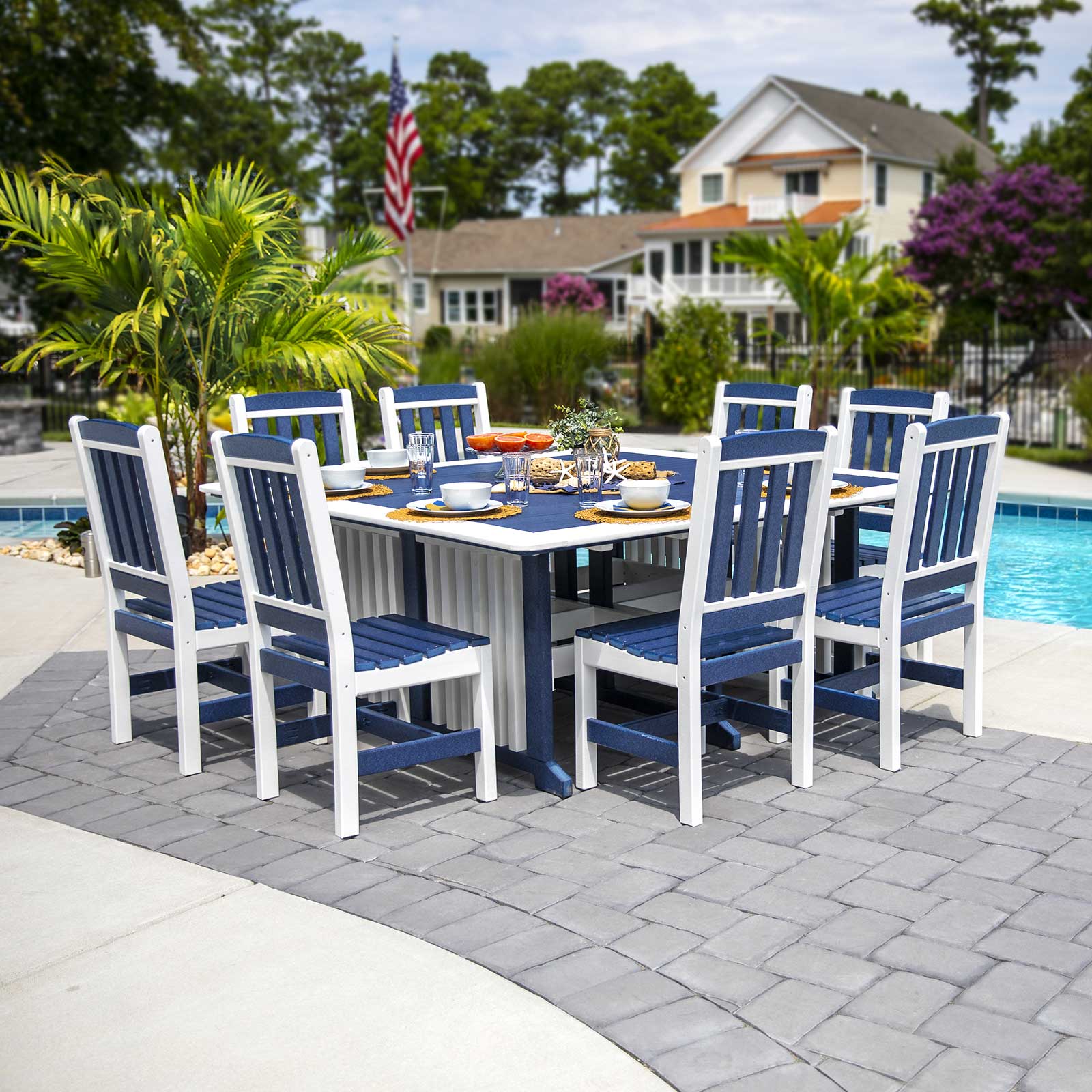 Navy blue and white poly square dining table with eight slat back chairs on a paver patio beside a pool