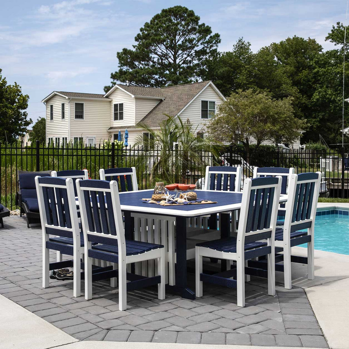 Candles, greenery and orange mimosas arranged on a navy poly patio dining table between white slat chairs