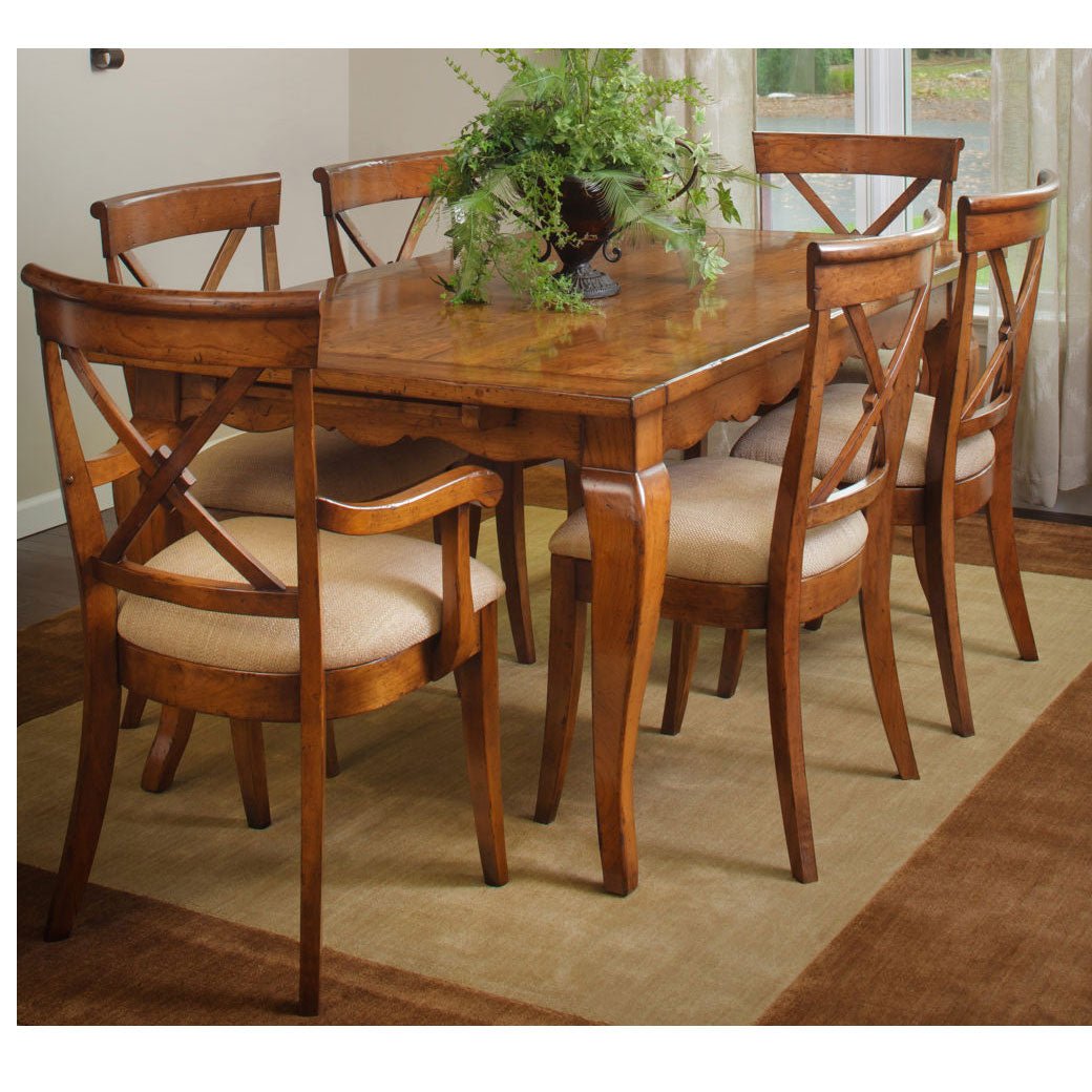 Wood dining table set for six with X-back side and arm chairs, linen seats and a fern centerpiece by a bright window