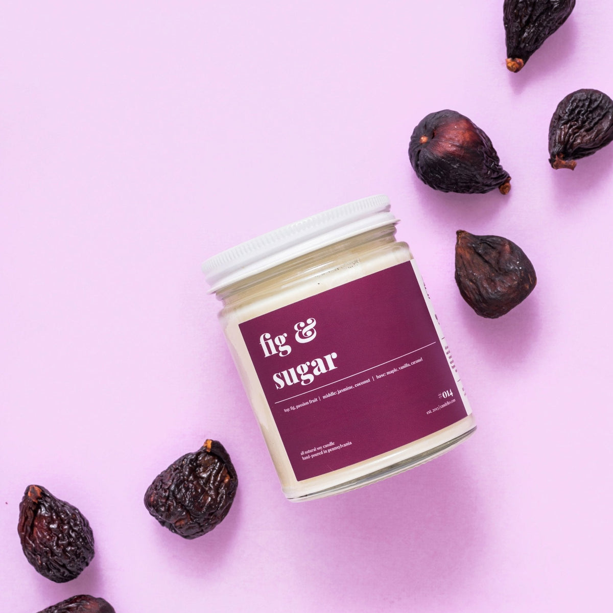 Fig and sugar soy candle with white lid photographed from above surrounded by scattered dried figs on lilac