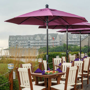 Waterfront dining tables with ivory slat back poly chairs, purple napkins and burgundy market umbrellas at dusk