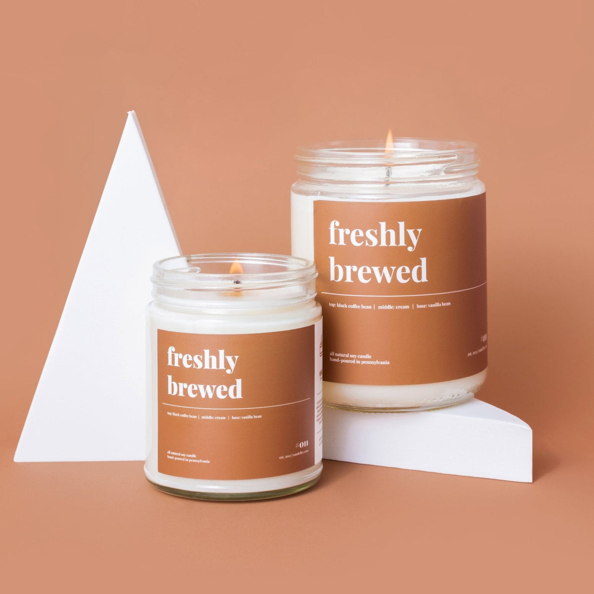 Petite and standard freshly brewed soy candles burning beside a white triangle prop on a terracotta backdrop