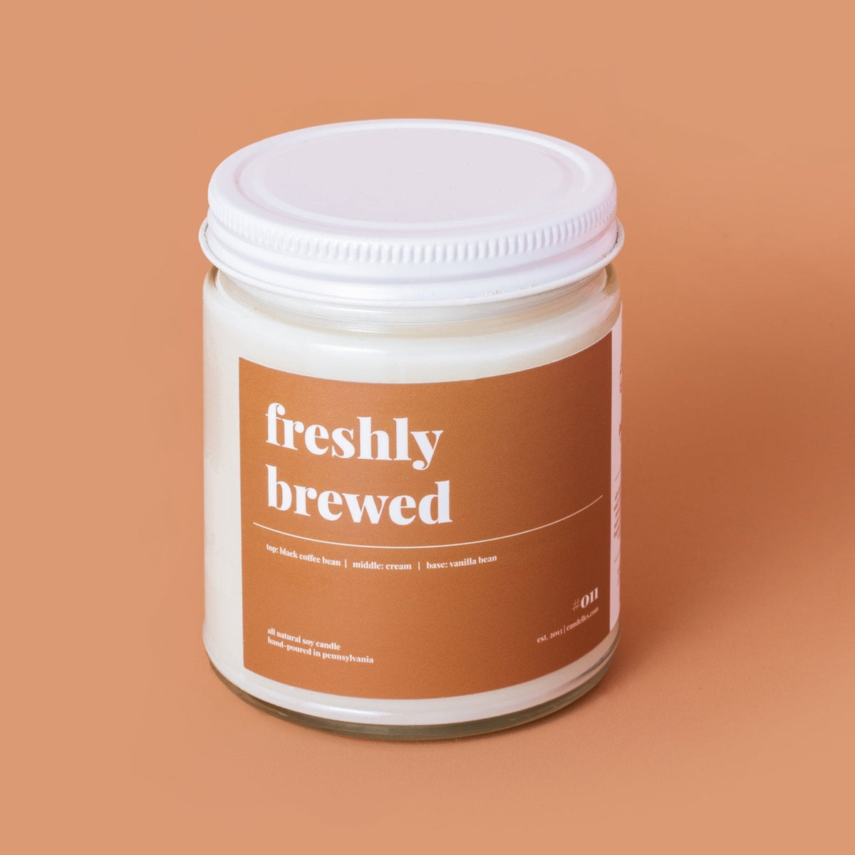 Freshly brewed coffee scented soy candle in a clear jar with brown label and white lid on a terracotta background