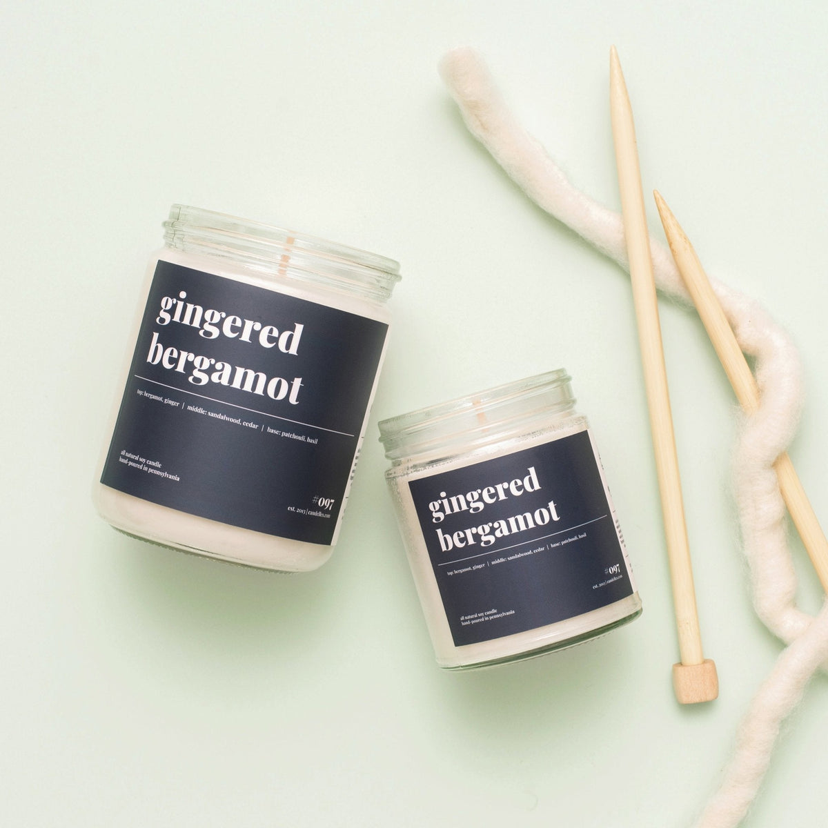 Standard and petite gingered bergamot soy candles with black labels beside knitting needles and yarn on mint