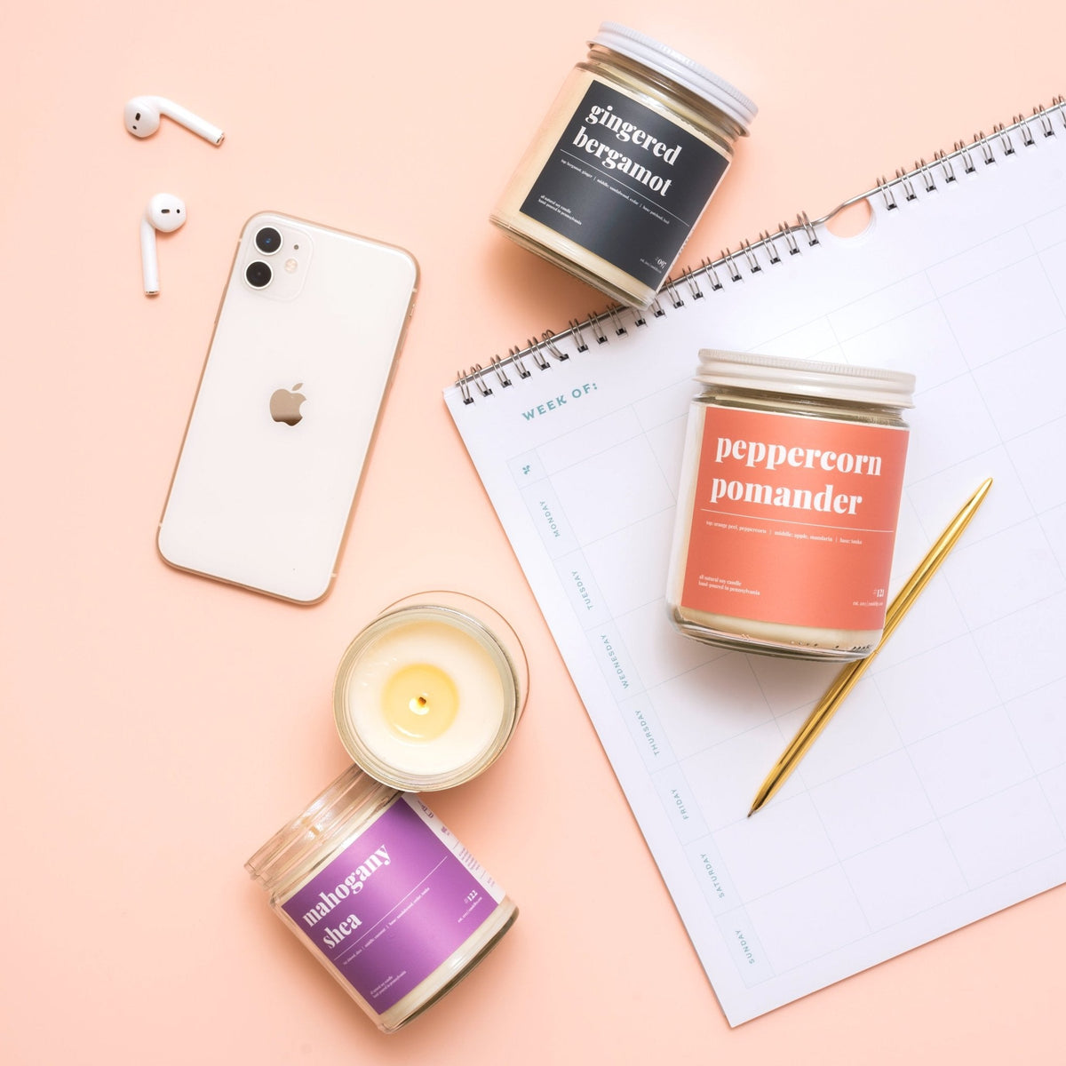Desk flat lay with gingered bergamot, peppercorn pomander and lit mahogany shea candles beside a phone and planner