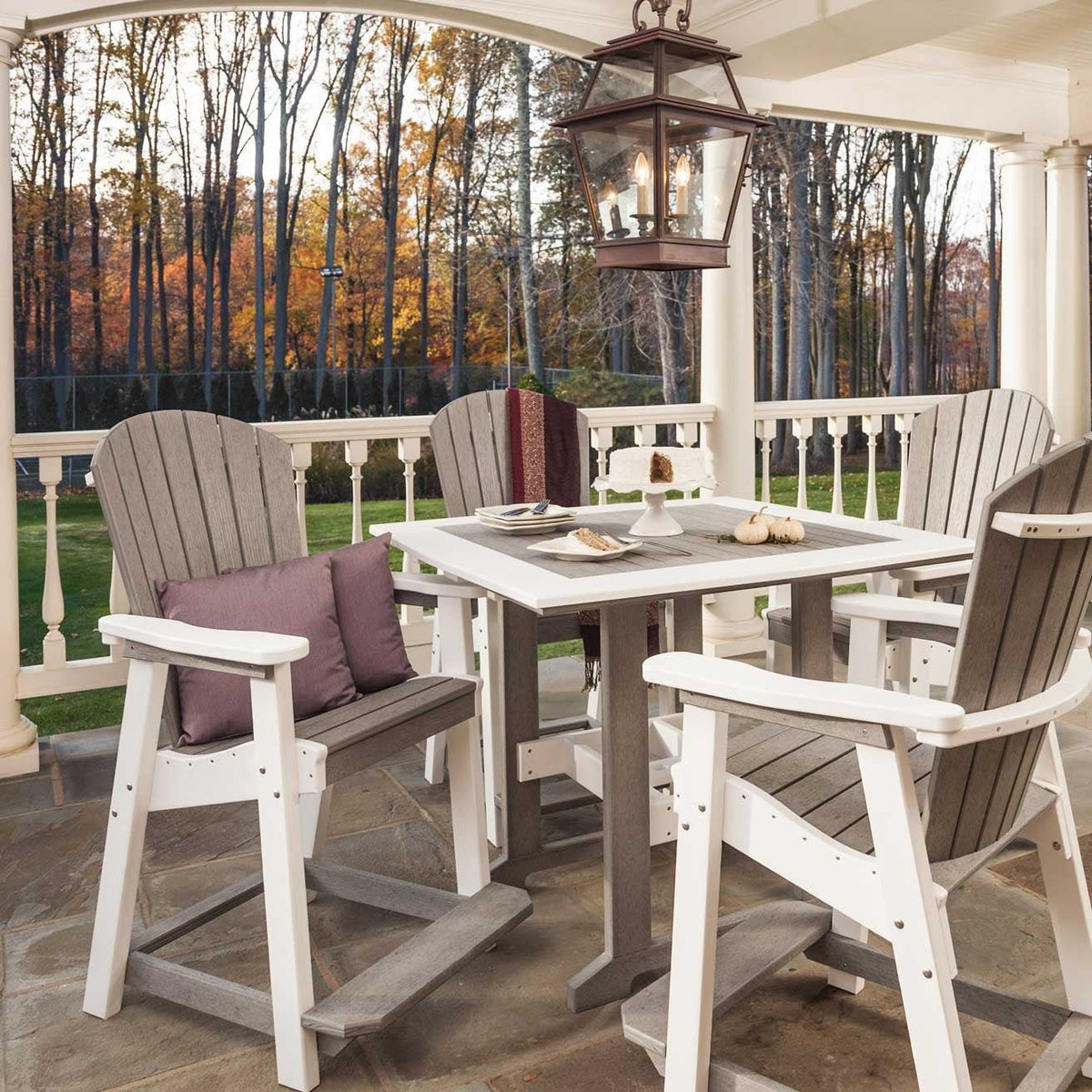 Driftwood gray and white poly bar table with four tall Adirondack chairs on a stone porch in autumn