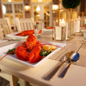 Lobster dinner plated on a driftwood poly patio dining table with candles and glassware at dusk