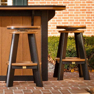 Two cedar and black poly swivel bar stools with round seats and footrests beside an outdoor bar on brick