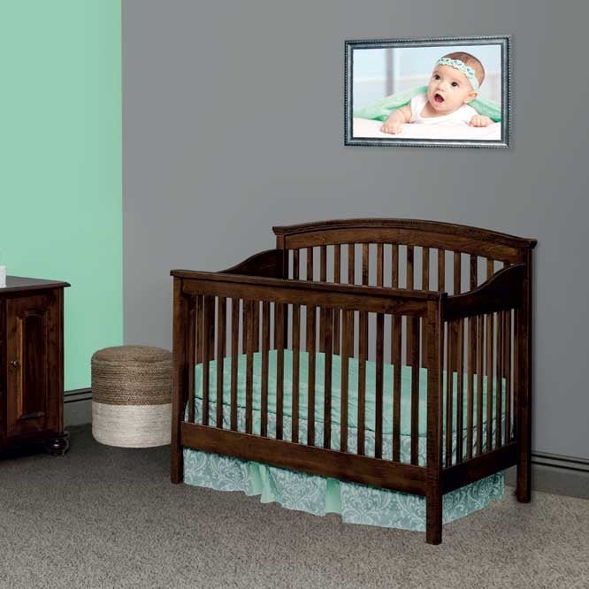 Espresso convertible crib with arched headboard styled against a gray and mint nursery wall with a woven ottoman
