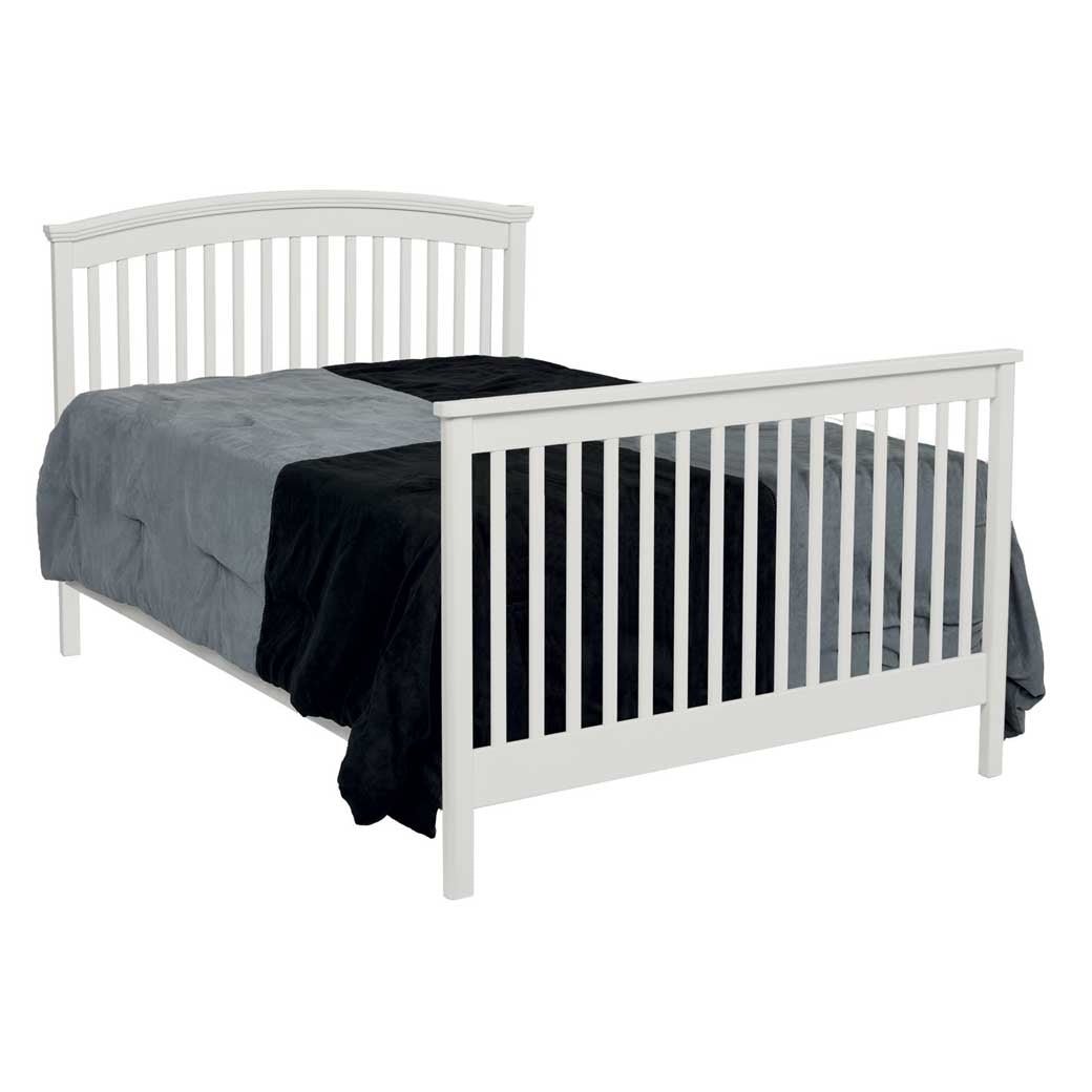 White convertible crib converted to a full bed with arched slat headboard, slatted footboard and gray bedding