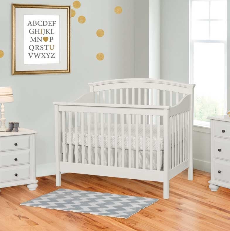 White painted convertible crib with an arched slat headboard in a gray nursery with a chevron rug and dresser