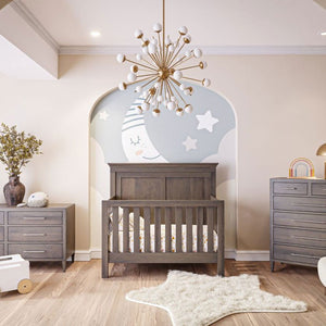 Gray stained panel crib styled in a nursery with matching dressers, moon mural and starburst chandelier