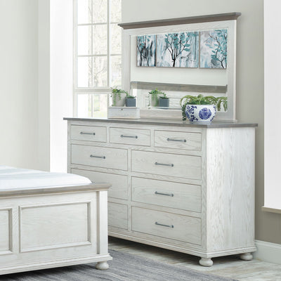 Whitewashed nine drawer dresser with gray top and wide mirror styled with plants beside a matching bed