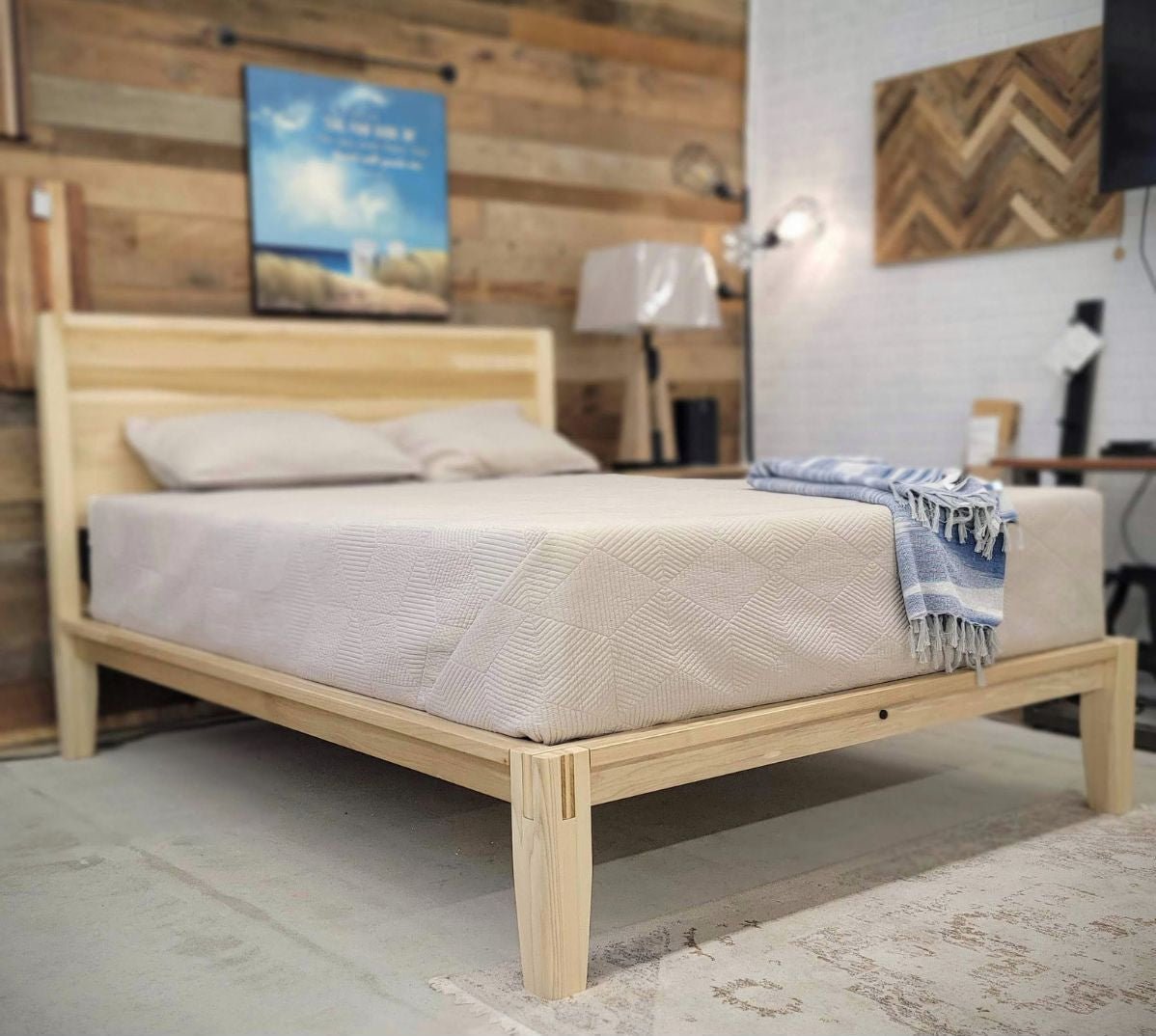 Light natural pine platform bed with slatted headboard panel and mattress, shown in a reclaimed barnwood showroom setting