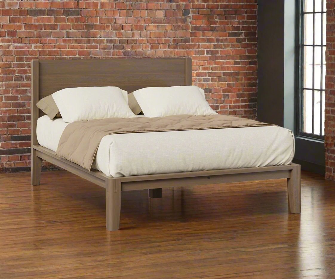 Weathered driftwood gray platform bed with plank panel headboard, staged against an exposed brick wall and hardwood floor