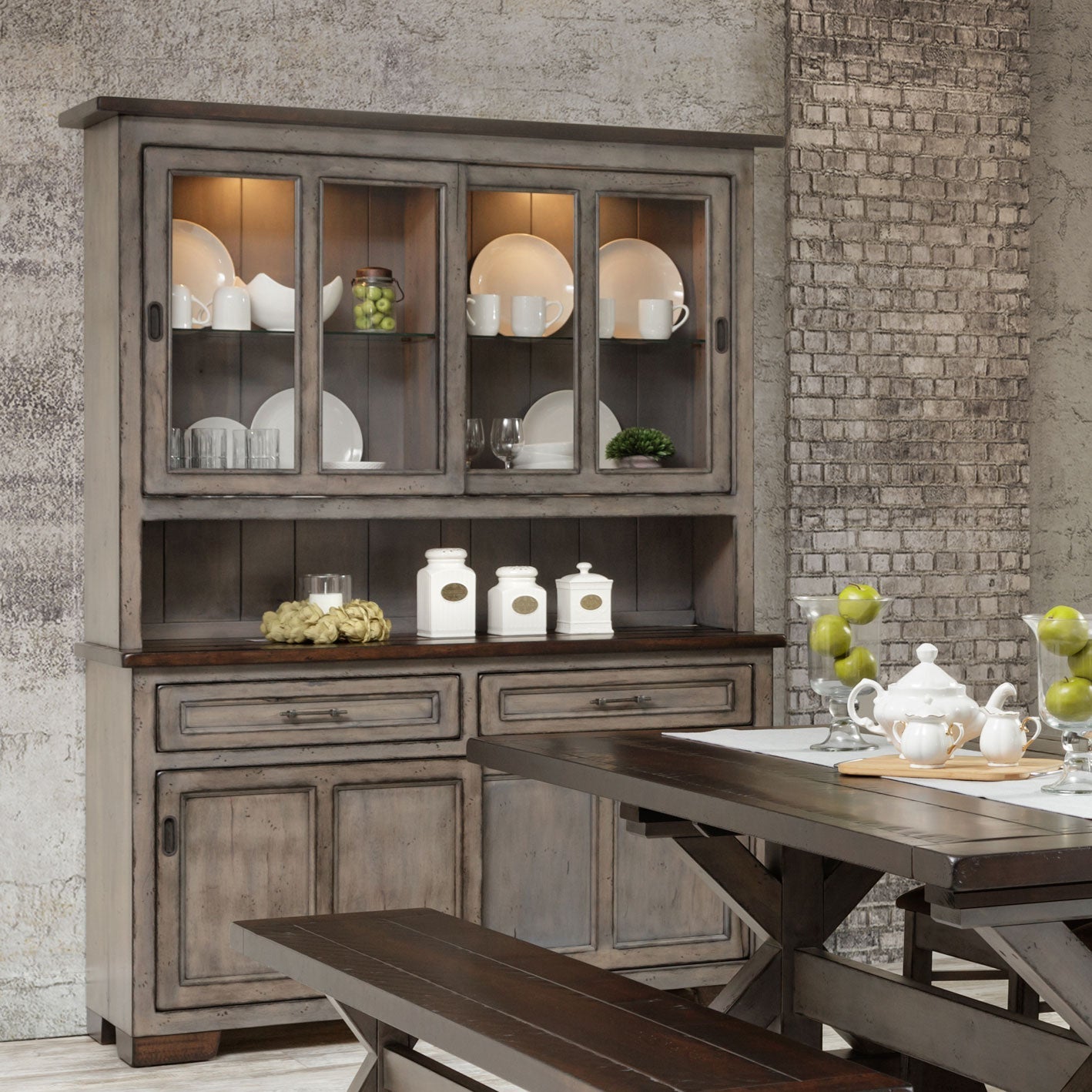 Weathered gray 63 inch hutch with lit sliding glass doors of white dishes, dark plank top and paneled base in a brick dining room