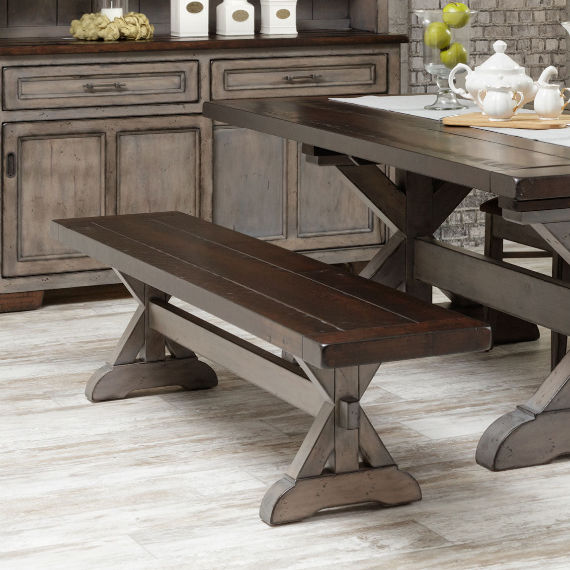 Dark walnut plank top dining bench on a gray X trestle base, placed alongside the trestle table and gray server