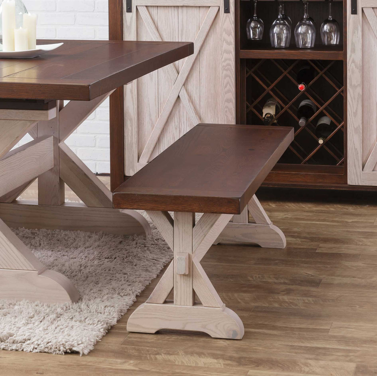 Walnut topped X base trestle dining bench with white washed base beside the matching table and wine cabinet