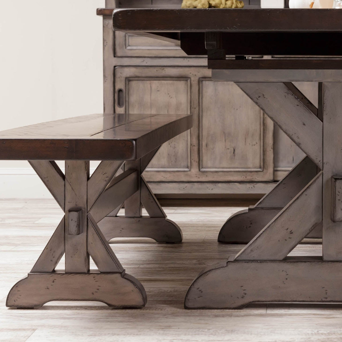 Close-up of the X trestle bench base in weathered gray with curved feet beside the matching dining table base