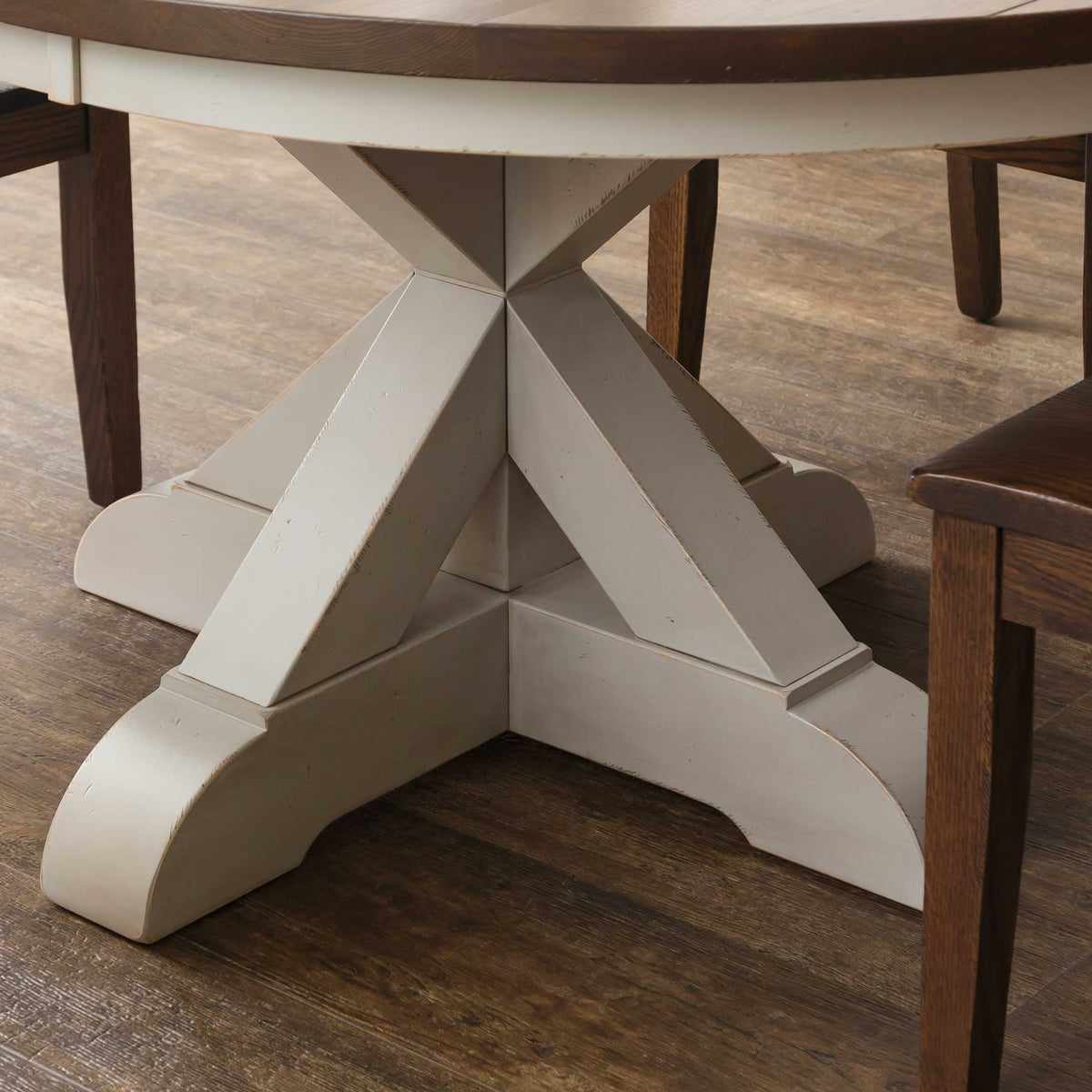 Detail of the cream X pedestal base with distressed edges and three scrolled feet under the round oak top
