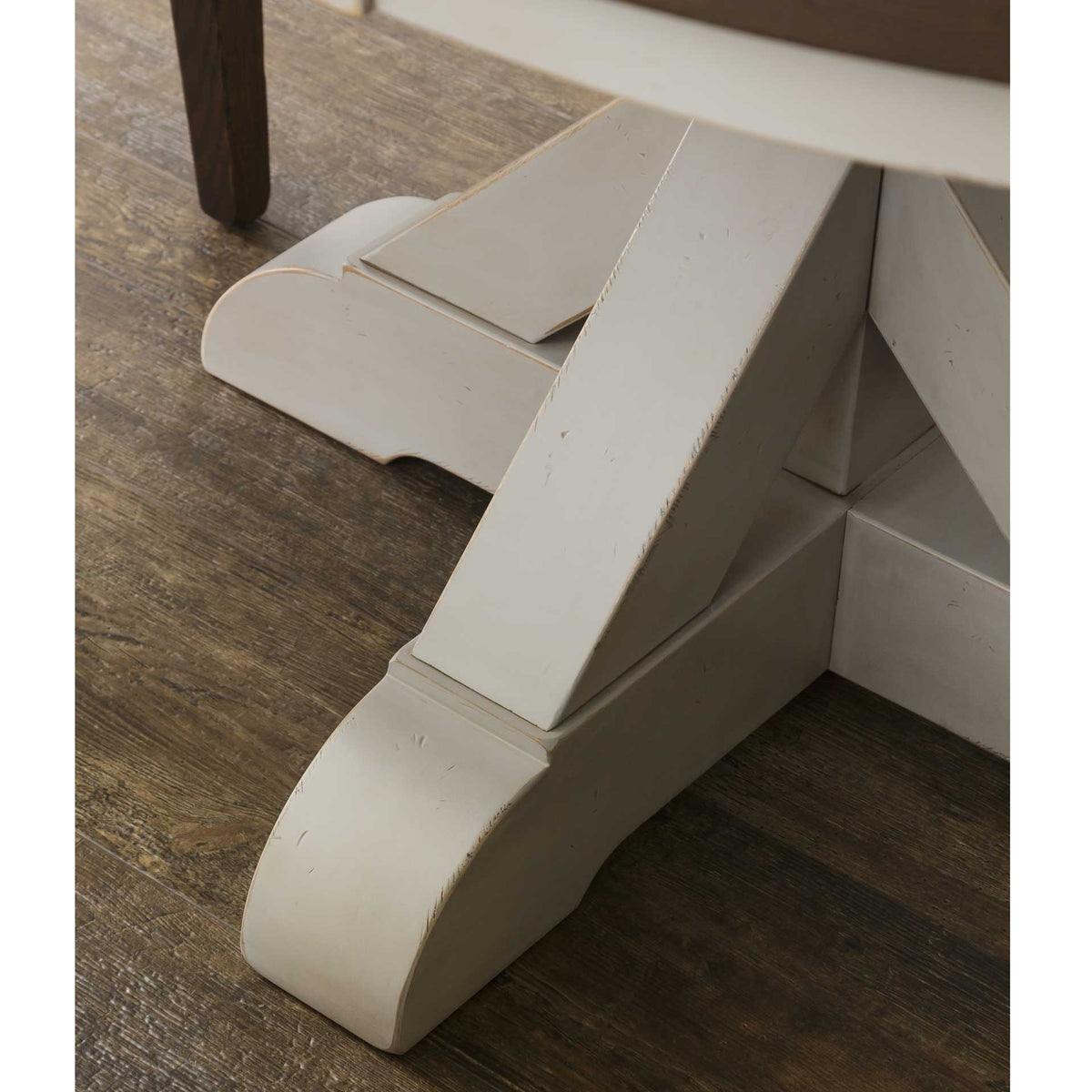 Detail of one scrolled foot on the cream painted pedestal base against rustic plank flooring