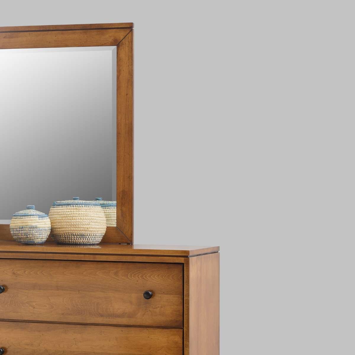 Close-up of the dresser's framed mirror and woven lidded baskets resting on the warm maple top against a gray wall