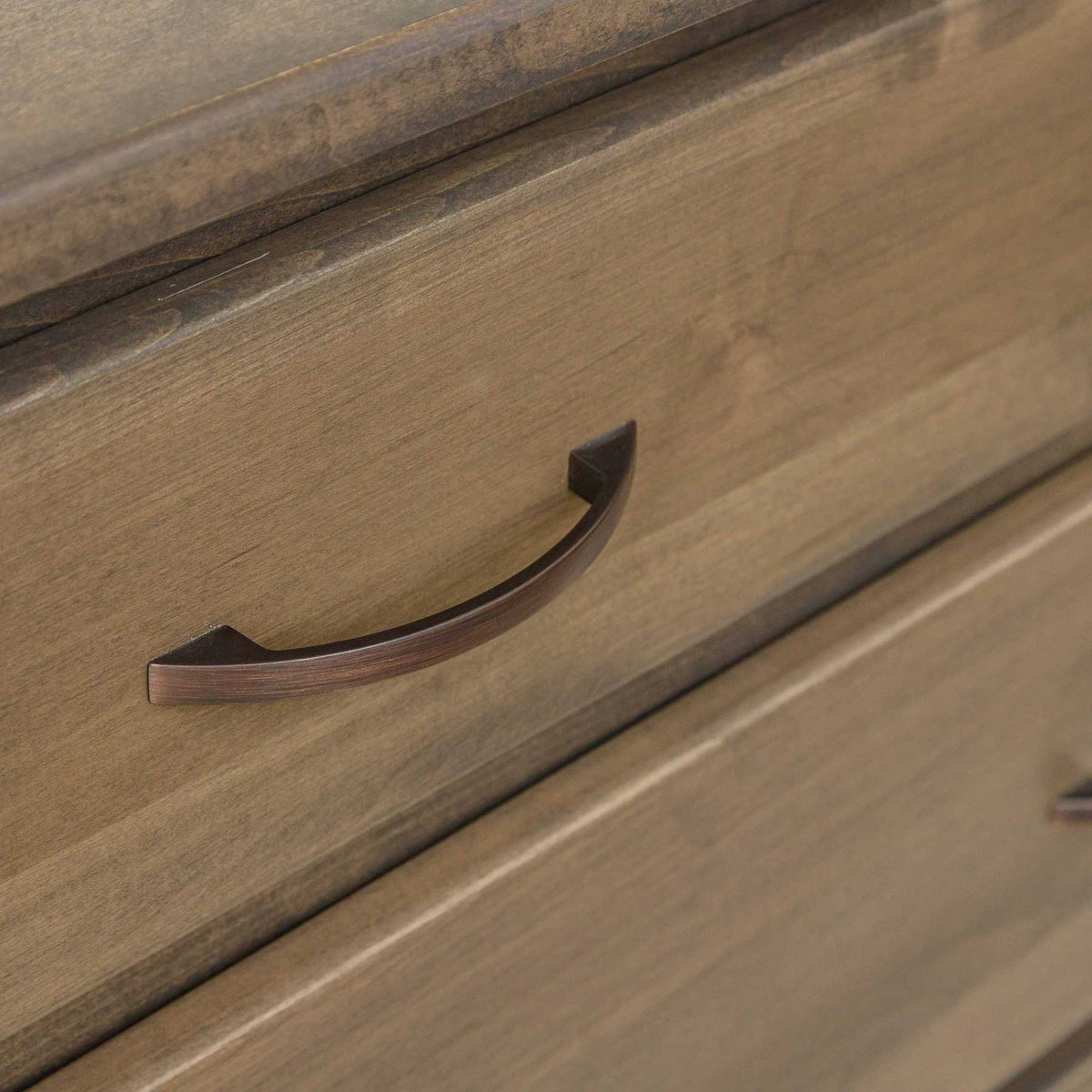 Close-up of the dresser's bronze arched drawer pull mounted on a smooth light stained drawer front