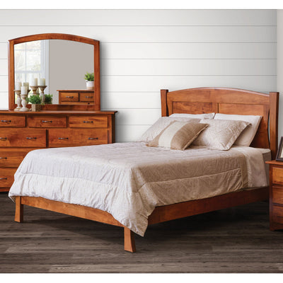 Modern arched panel bed in warm cherry with curved posts and low footboard beside a mirrored dresser