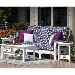 White poly outdoor sofa with navy patterned cushions and purple pillows, flanked by end tables and a coffee table