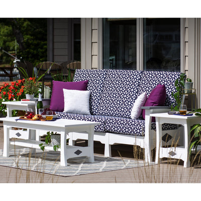 White poly outdoor sofa with navy patterned cushions and purple pillows, flanked by end tables and a coffee table