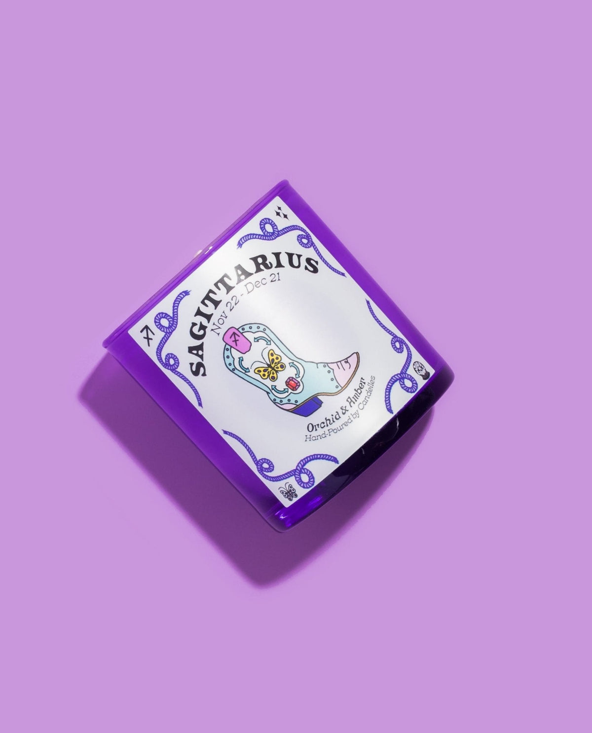 Sagittarius orchid and amber candle tilted on lilac, showing the butterfly detailed cowboy boot label artwork