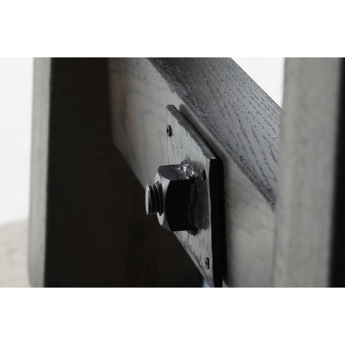 Iron buckle plate with hex nut bolting the angled trestle leg to the base of the gray dining table